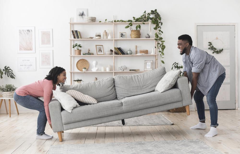 Happy african american couple moving sofa in living room, replacing furniture at home, side view